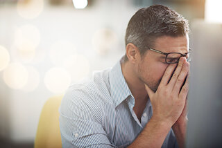 Erschöpfter Mann mit Brille hält sich die Augen @ 