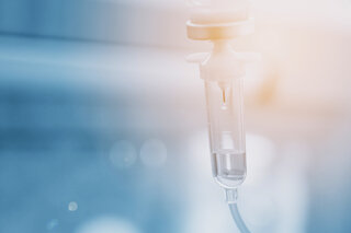 Infusionsbeutel mit Tropfen vor blauem Klinik-Hintergrund @ 